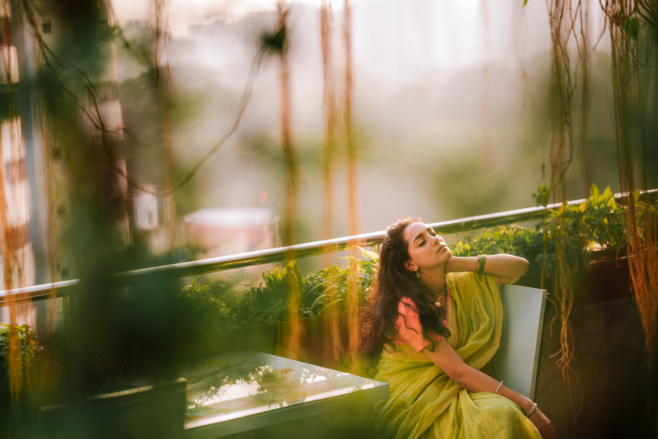 A young woman in a green sari enjoying a peaceful moment on a sunlit balcony.