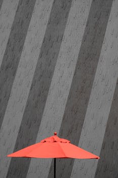 Bold red umbrella contrasts sharply with a geometric patterned grey wall in a minimalist style.