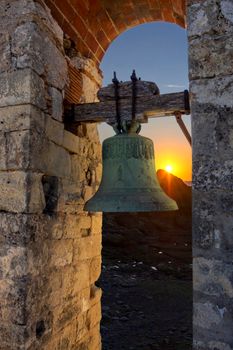 A rustic bell hangs in stone archway at sunset in Laviana, Spain, capturing historic charm.