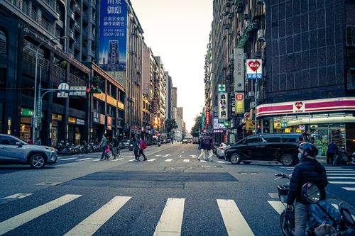 Free Pedestrians and vehicles navigate a busy Taipei street crossing at dusk, showcasing urban life. Stock Photo