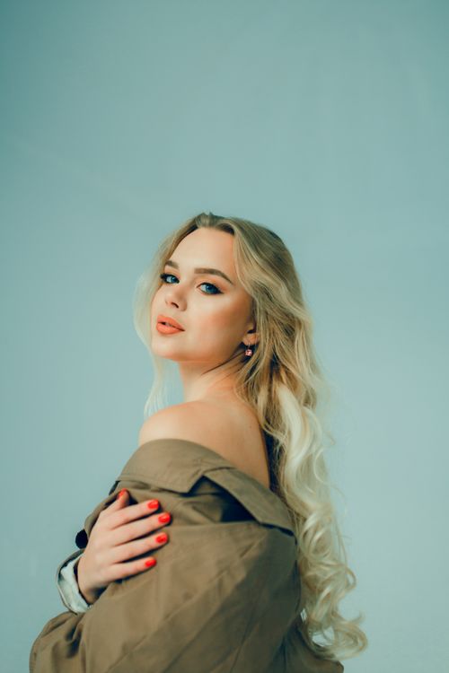 Free Elegant portrait of a blonde woman with bare shoulder against a green background. Stock Photo