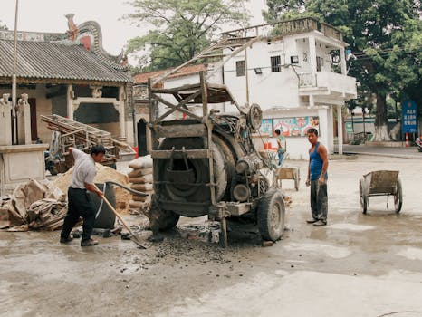 Two workers operating cement mixer in outdoor construction setting.