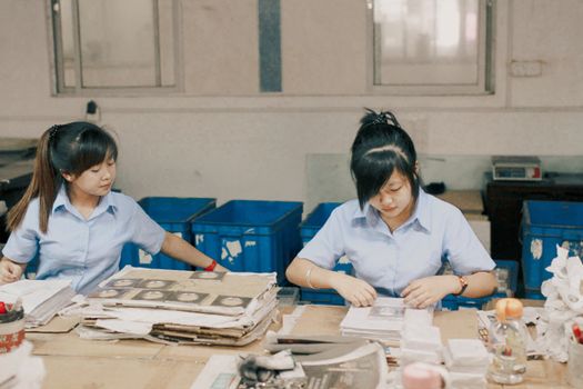 Two women organizing materials at a work table in an industrial plant setting.