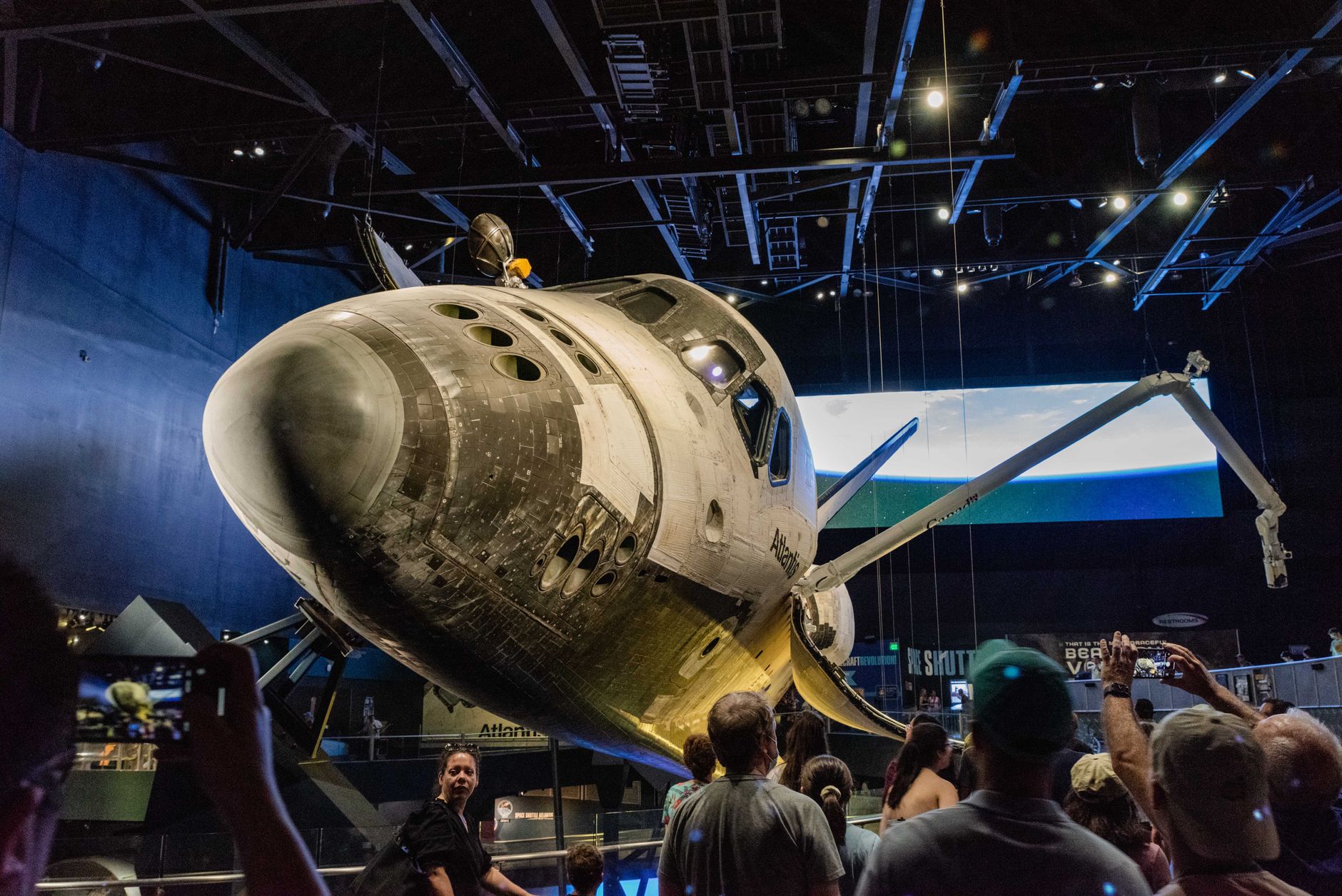 Crowd admires Space Shuttle Atlantis at an indoor space museum exhibit.