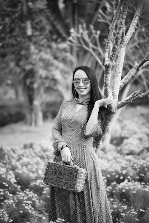 Grayscale Photo of Woman in Polka Dot Dress Standing beside Tree