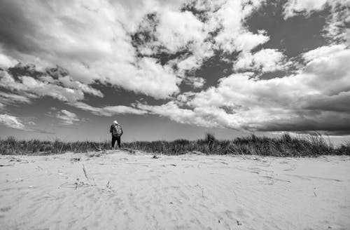 Black and White Photo of Man with a Backpack Standing on a Beach 