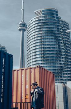 Person in jacket near containers with CN Tower backdrop in Toronto.