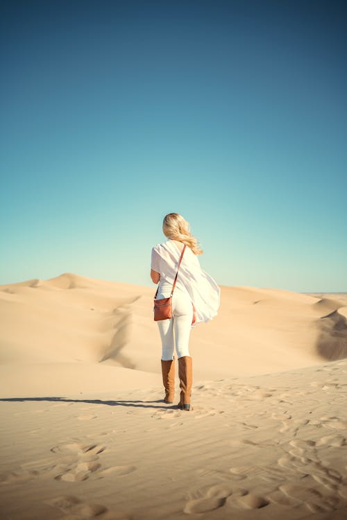 Woman Walking on Dunes Under Blue Sky 