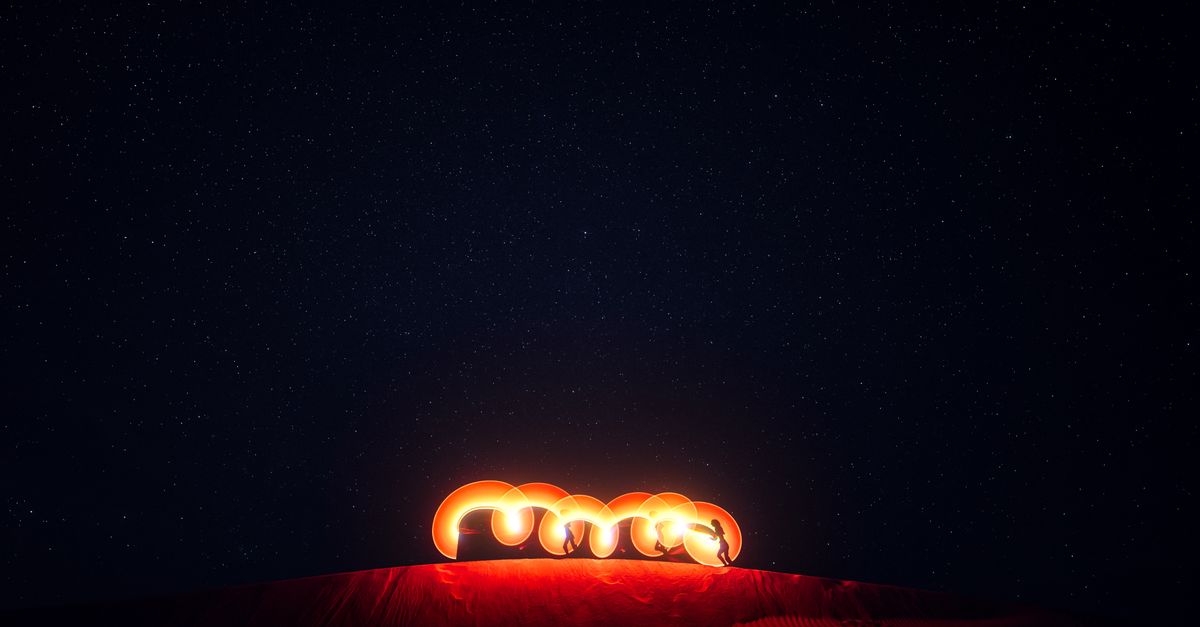 A captivating fire performance under the vibrant starry night sky in a desert landscape.