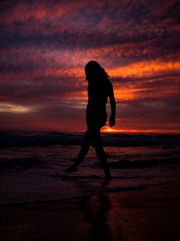 A silhouette walking along the beach at sunset with vibrant sky colors.