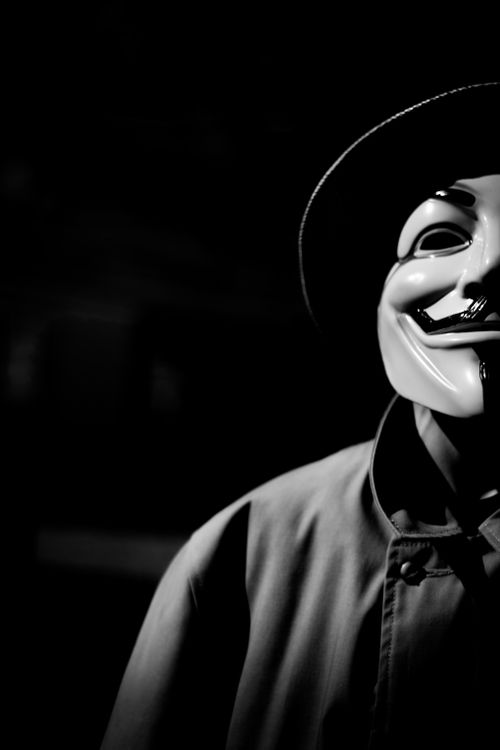 Free A mysterious figure wearing a mask and coat stands in shadow, creating an eerie ambiance. Stock Photo