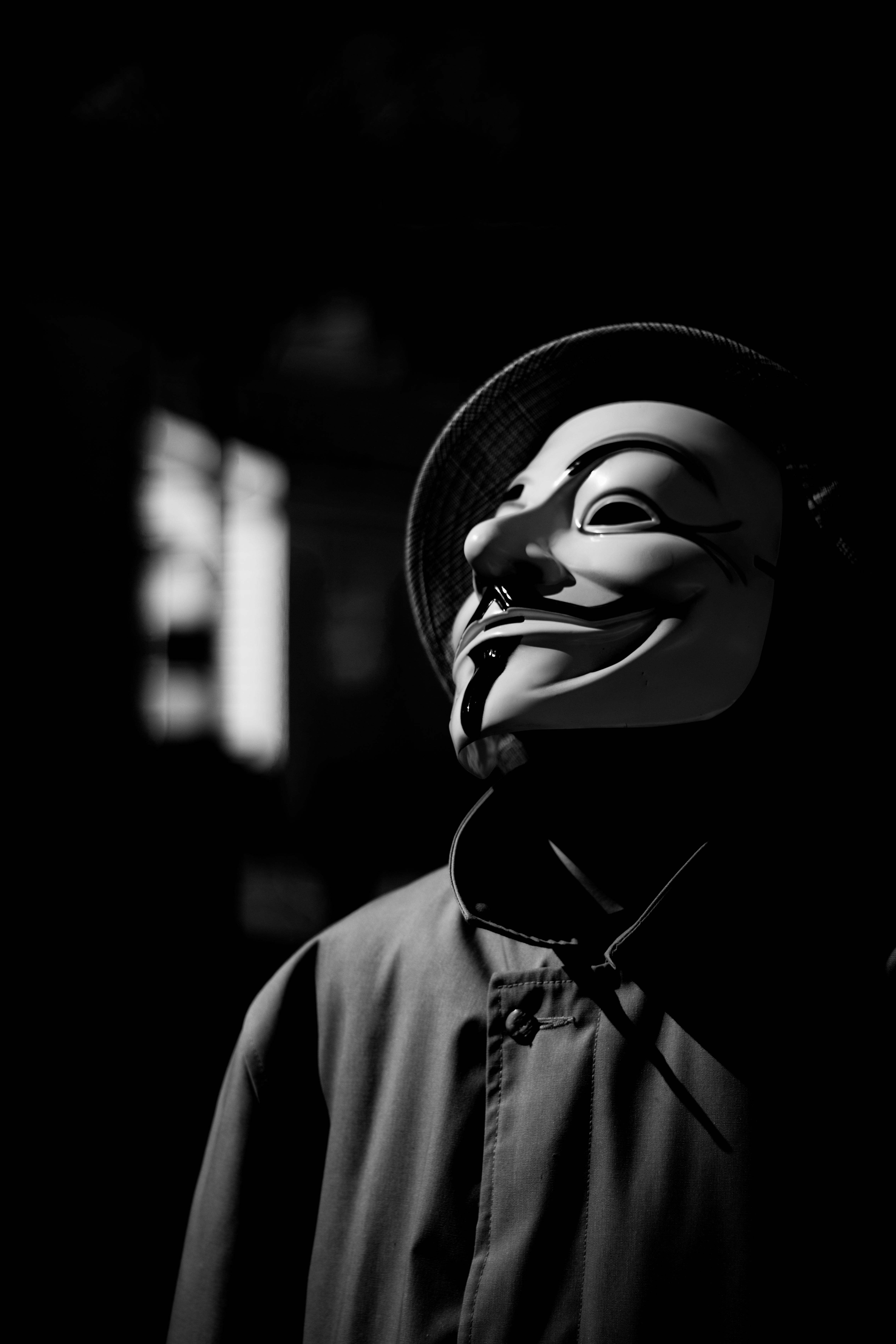Free A person wearing a Guy Fawkes mask in a dramatic black-and-white photograph. Stock Photo
