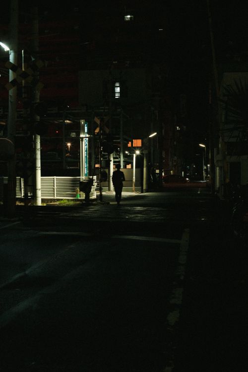 Free Silhouette of a lone figure walking through a dark urban alley at night. Stock Photo