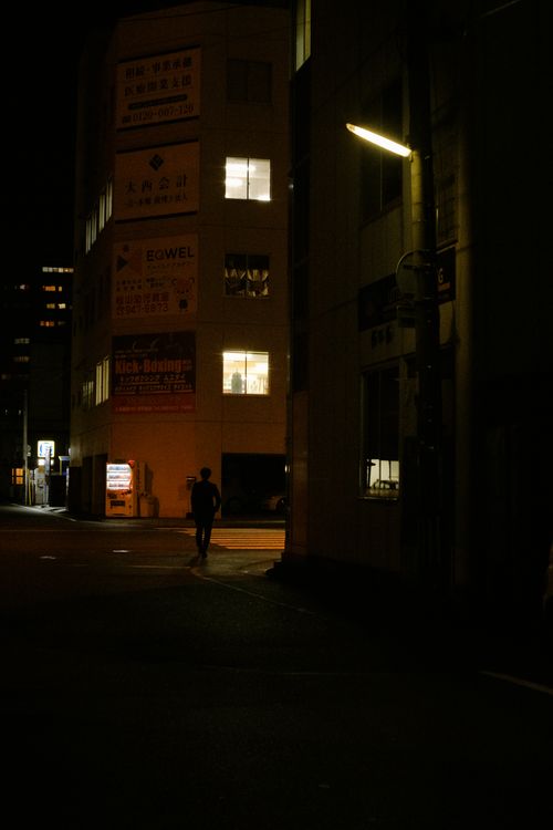 Free Silhouette of a person walking on a dimly lit urban street at night. Stock Photo