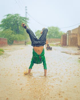 A man in green performs a handstand on a flooded street in Pakistan during a rainstorm.