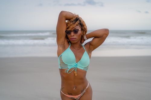 Free A young woman in a bikini enjoys the beach, with arms raised, exuding confidence. Stock Photo