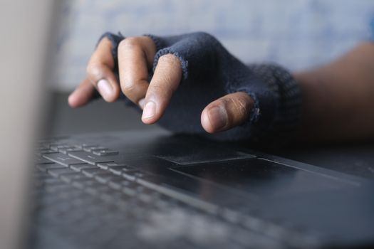 A person in gloves typing on a laptop keyboard, focusing on hands and keys in a dim-lit setting.