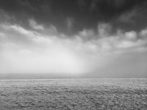 Grayscale Photo of Hayfield under Cloudy Sky 