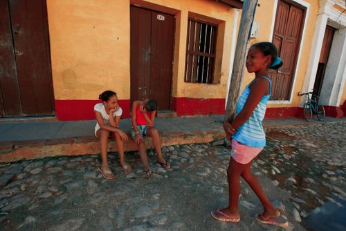 Free Three children share a joyful moment outdoors on a sunlit cobblestone street. Stock Photo