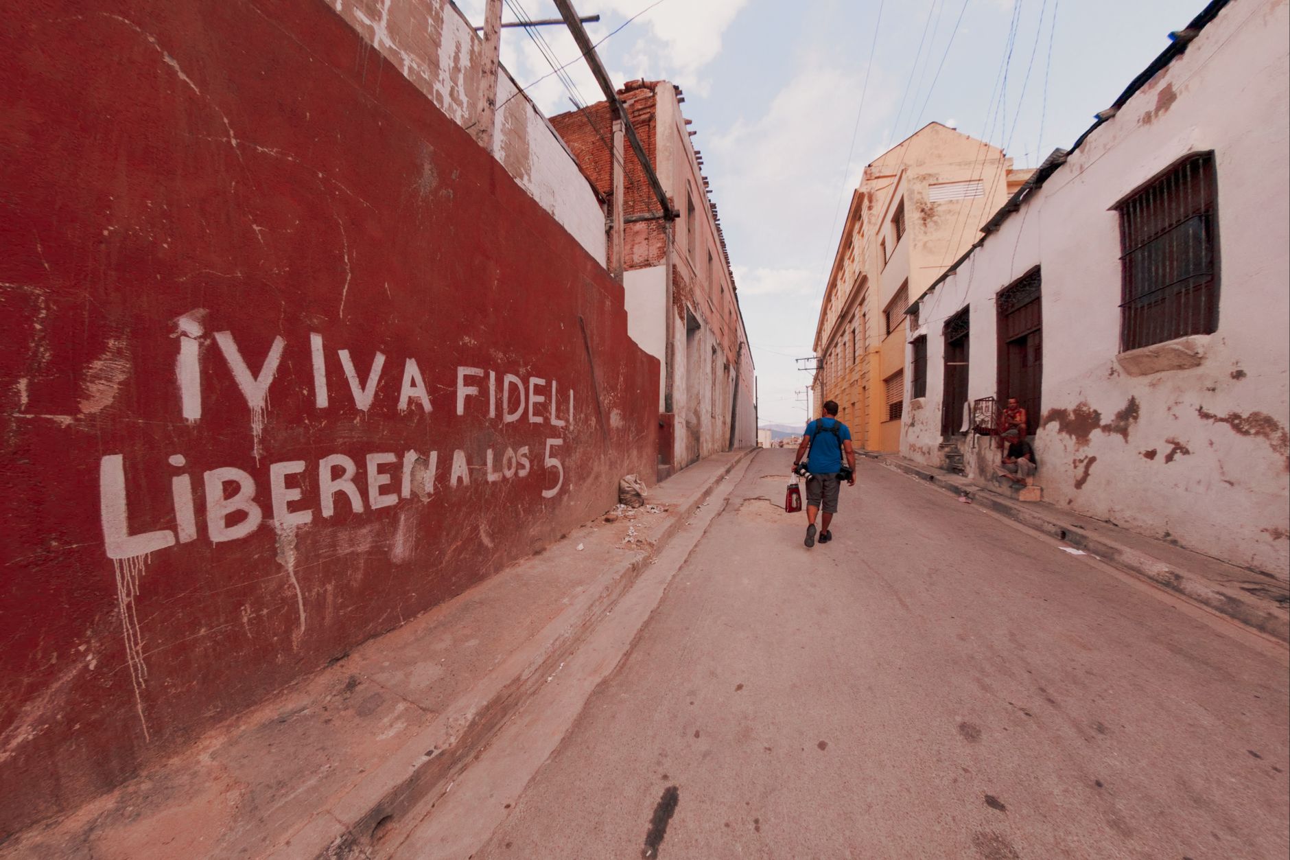 A man in a blue shirt walks along an alley with political graffiti on the wall.