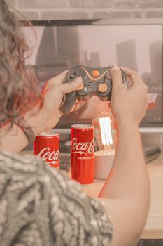 Over-the-shoulder view of a person playing video games with a controller, surrounded by soda cans.