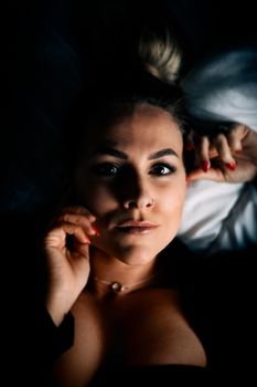 Dramatic portrait of a woman lying down, expressive eyes, soft lighting.