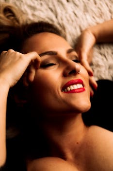 Joyful woman with vibrant red lipstick smiling indoors, showcasing beauty and relaxation.