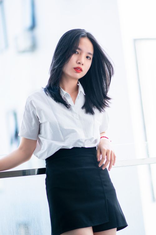 Free Chic young woman in a black skirt and white blouse posing indoors with confident elegance. Stock Photo