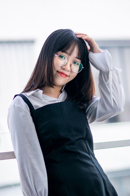 Charming portrait of an Asian teen smiling with hand on head, wearing eyeglasses.