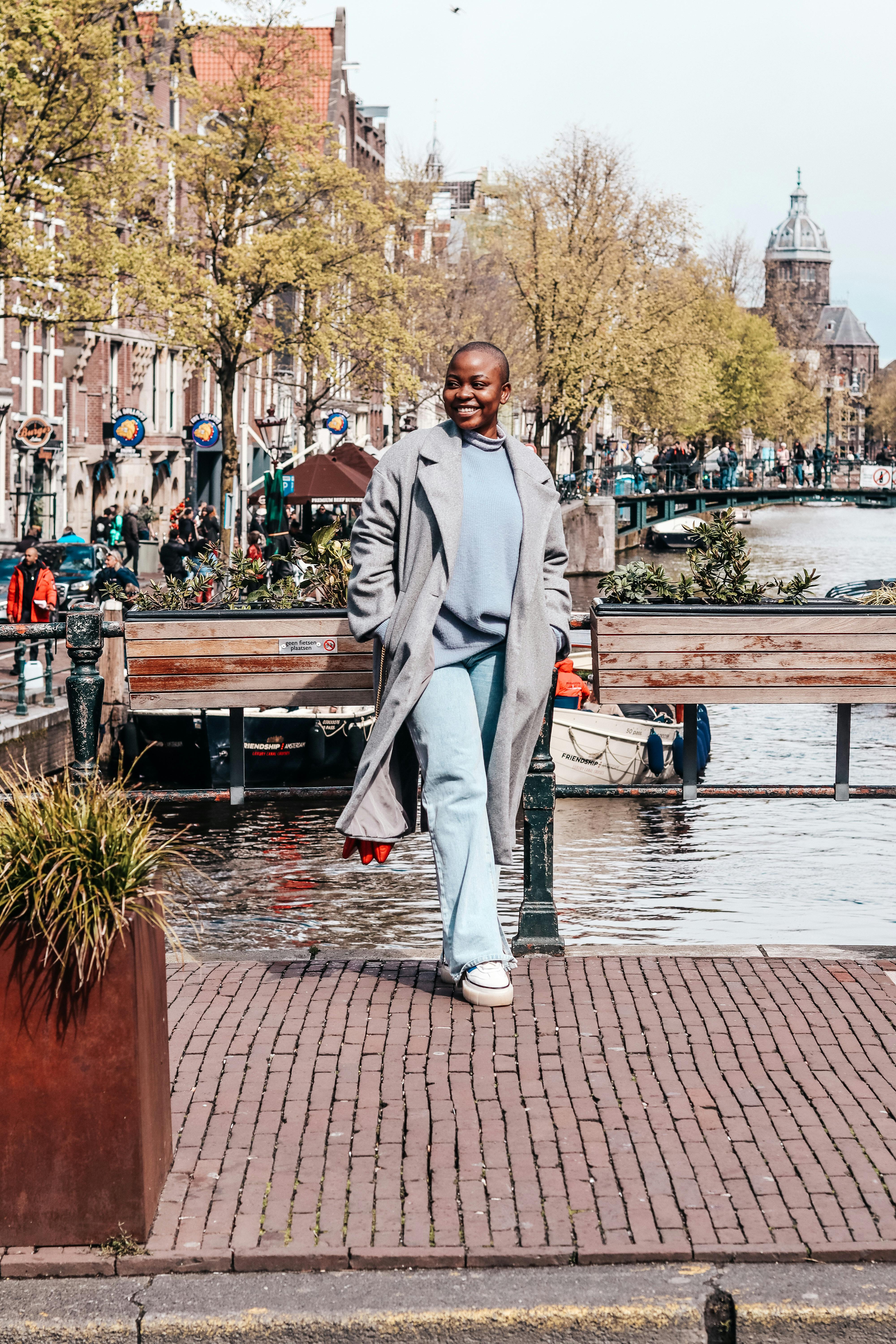 Confident woman in stylish coat walks by the scenic canal in Amsterdam during spring.