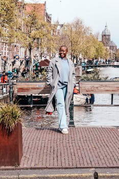 Confident woman in stylish coat walks by the scenic canal in Amsterdam during spring.