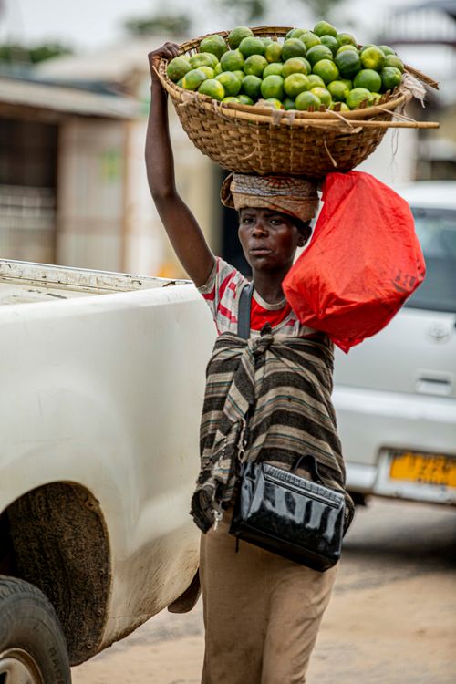 Free African street vendor carrying a basket of limes and a red bag, showcasing vibrant marketplace culture. Stock Photo