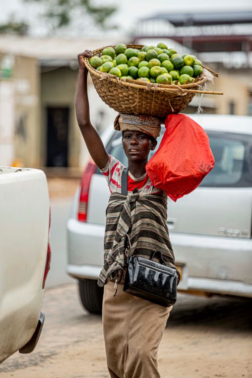 Free Street vendor carries a basket of green limes, portraying daily livelihood in an outdoor urban setting. Stock Photo
