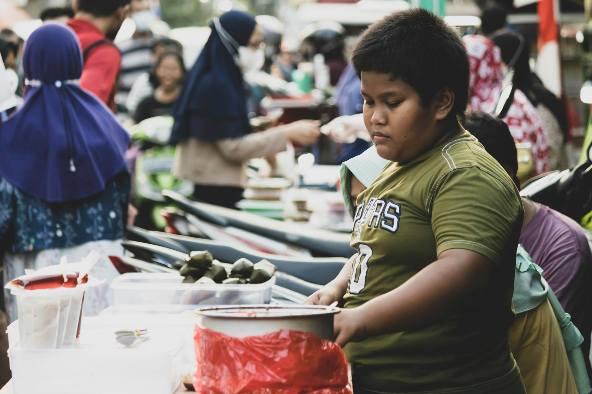 Young boy working at a busy street market, engaging with customers.