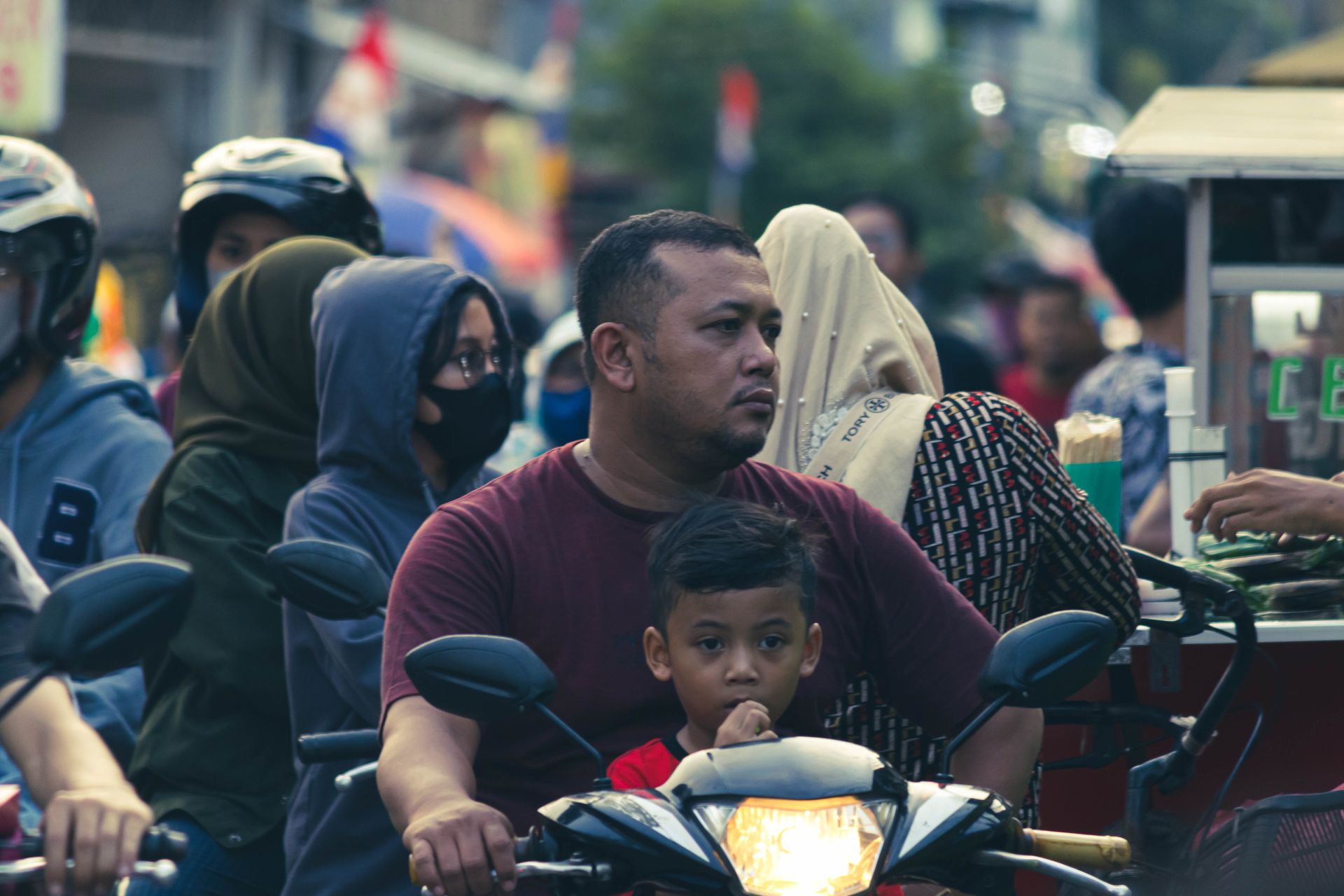 A father and son navigate a crowded street on a motorcycle, highlighting daily urban life.