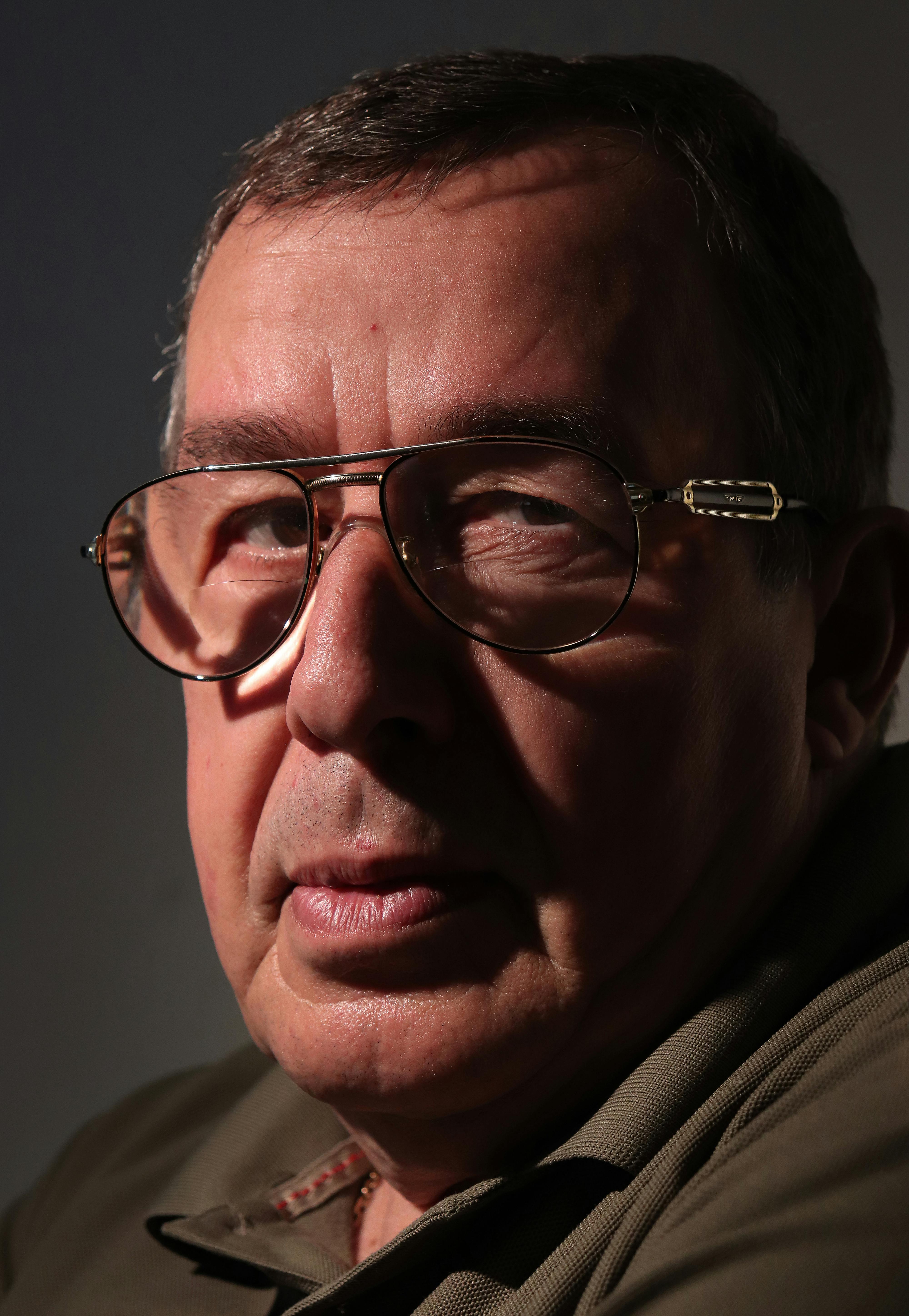 Close-up portrait of a mature man wearing eyeglasses with dramatic shadows on his face.
