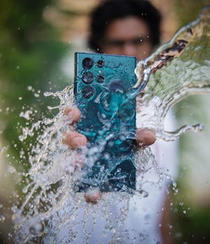 Close-up shot of a smartphone in hand with water splash effect, showcasing durability and technology.
