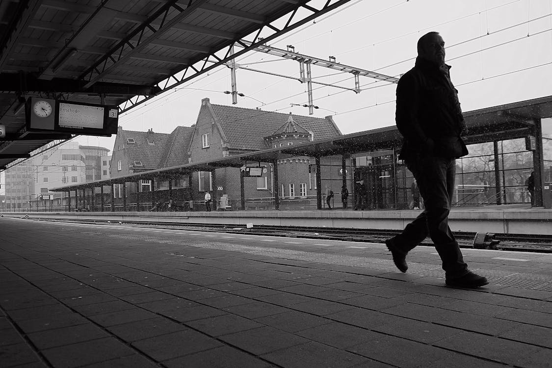 Grayscale Photo of Man Walking on Train Platform