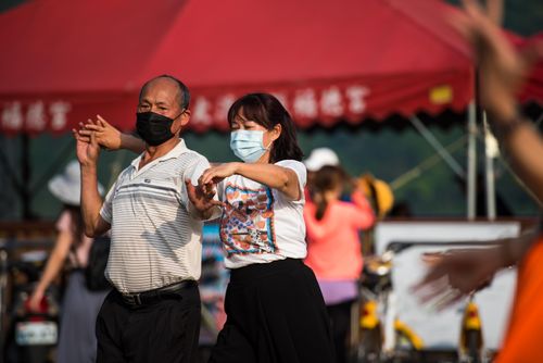 Free An adult couple wearing face masks dances outdoors amid new normal routines, highlighting adaptation to safety measures. Stock Photo