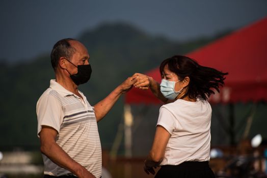 An elderly couple enjoying a dance outdoors while wearing face masks under a canopy.
