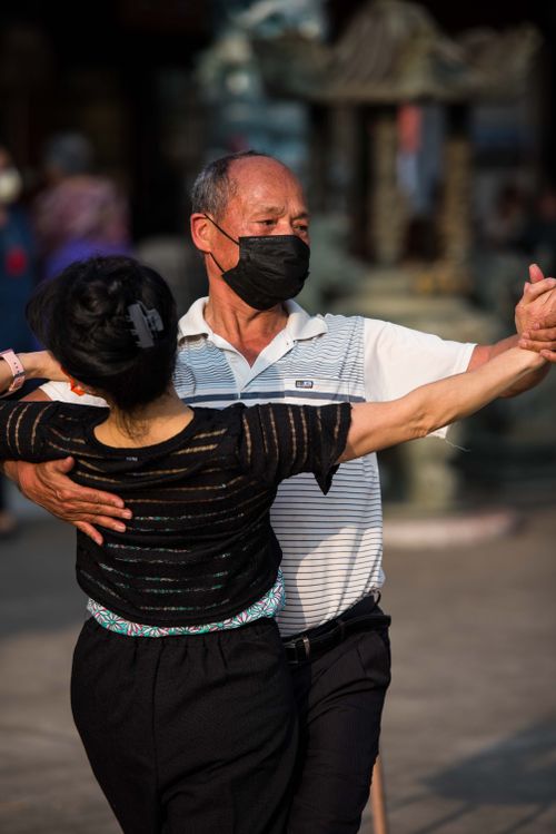 Free Elderly Asian couple dancing gracefully outdoors, enjoying a vibrant city atmosphere. Stock Photo