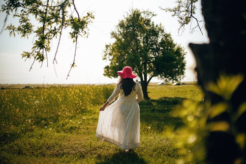 Woman in White Dress and Red Sunhat Standing on Green Grass Field