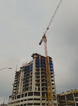 Low-angle view of a skyscraper under construction with a tower crane on a cloudy day.