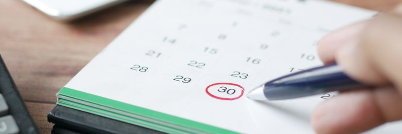 Close-up shot of a hand marking a date on a calendar with a pen, emphasizing planning and scheduling.