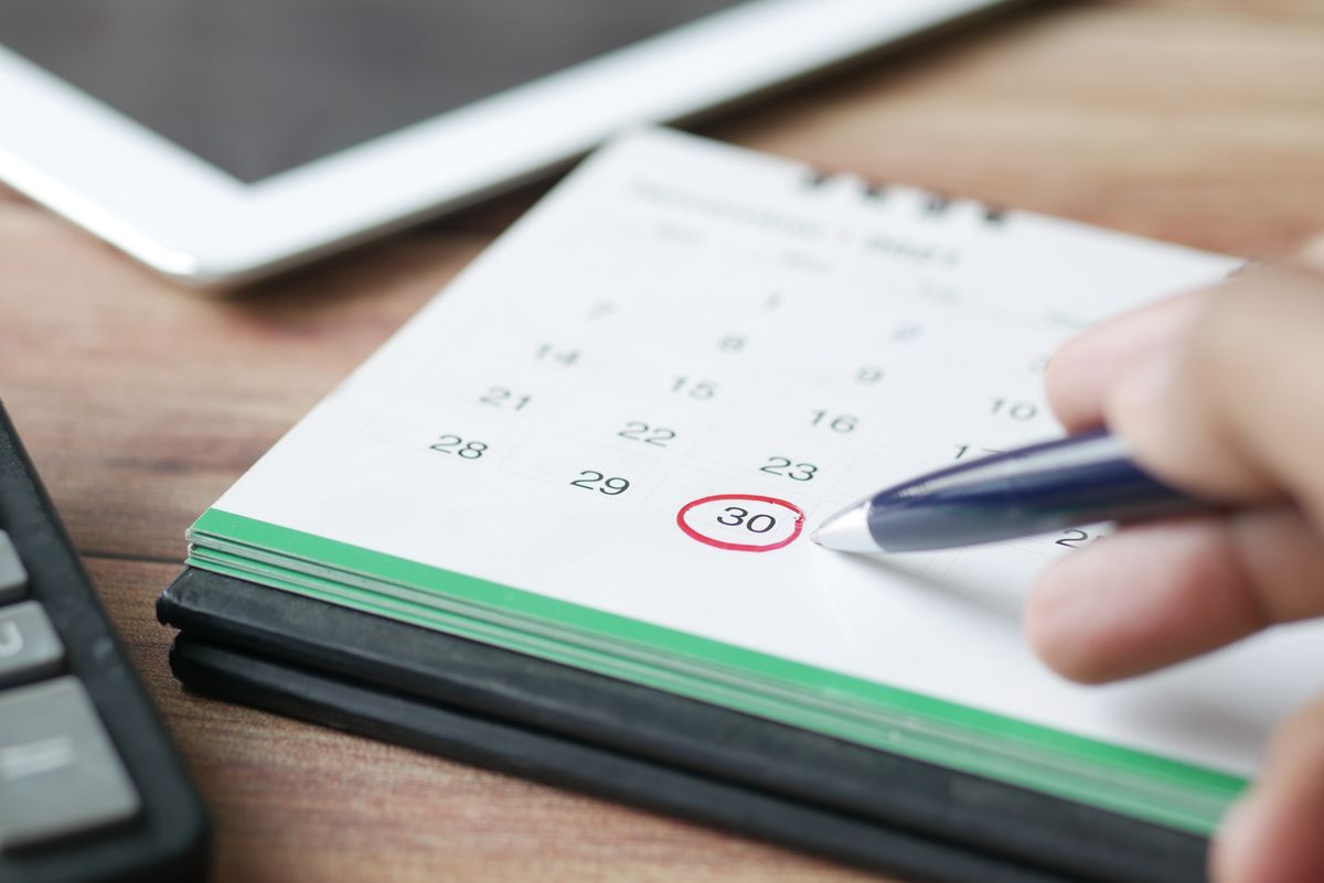 Hand marking a date on a calendar with a pen