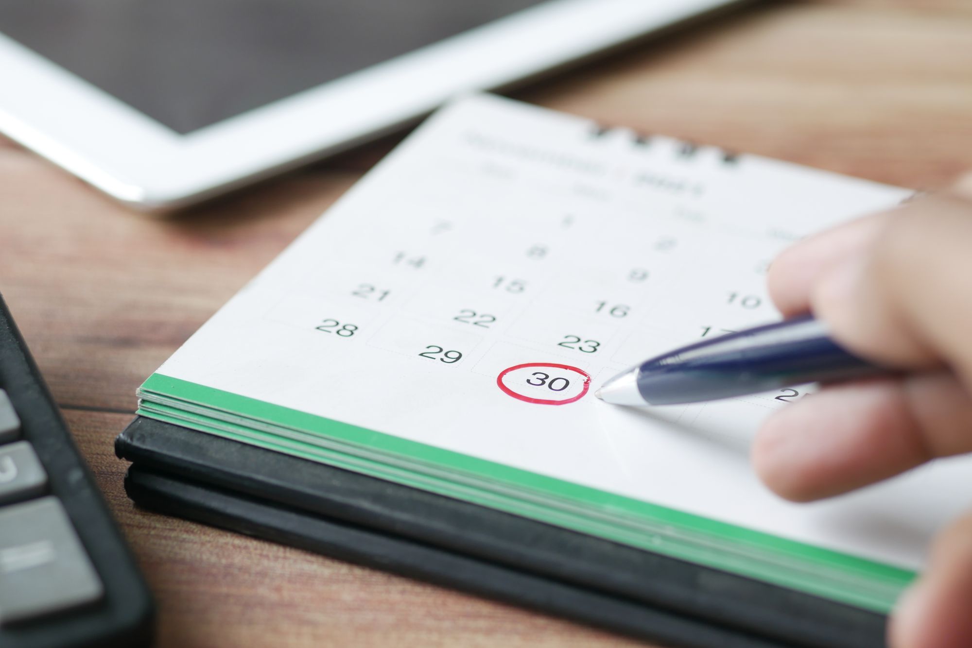 A hand circling a date on a desk calendar, planning around the cheapest time to charter a private jet