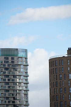 Contemporary skyscrapers with glass facades set against a bright blue sky with clouds.