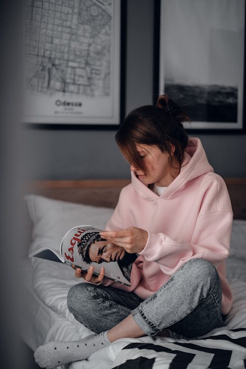 Free A Woman in Pink Hoodie Reading Magazine on Bed Stock Photo