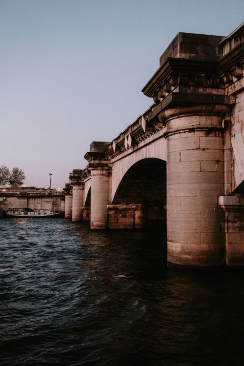 Free A majestic stone bridge arches over a rippling river under a serene evening sky. Stock Photo