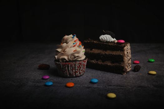 Close-up of a chocolate cake slice and cupcake with sprinkles and candies, perfect for sweet cravings.
